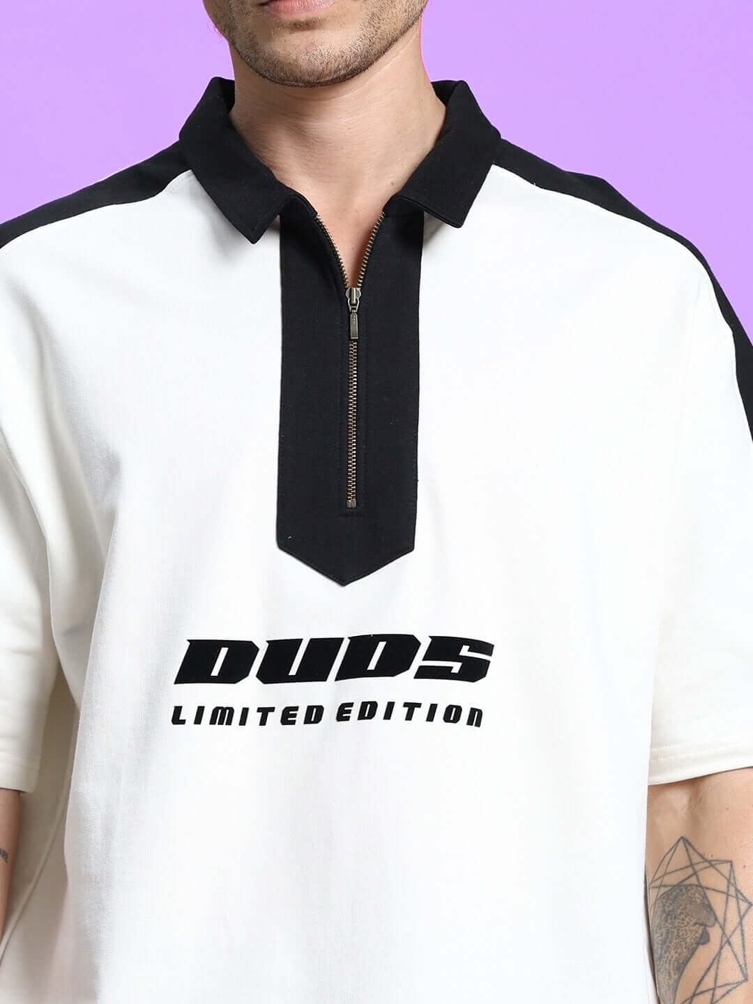 Close-up of a white co-ord set polo with a black zipper and 'DUDS Limited Edition' text, featuring black accents on shoulders, against purple background.