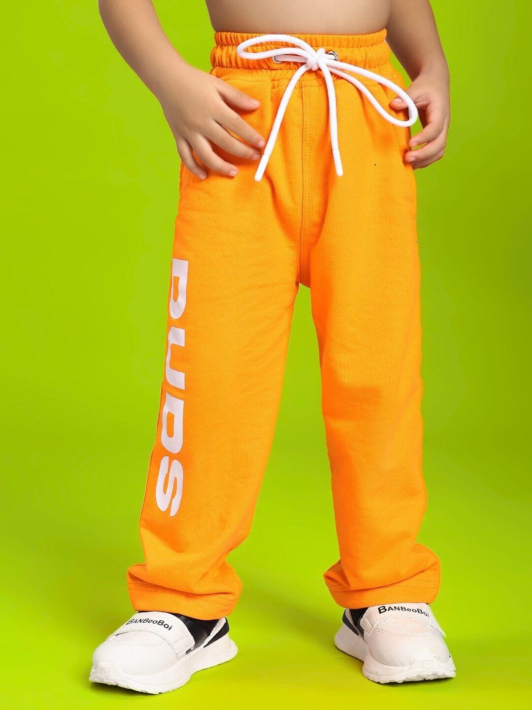 Child wearing LIMITED EDITION JOGGER FOR BOYS AND GIRLS ORANGE, showcasing vibrant orange pants with white drawstring on green background.