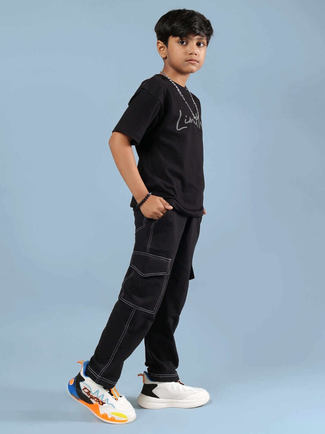Young boy wearing LIMITLESS CO-ORD FOR BOYS GIRLS BLACK standing against a blue background, showcasing stylish and comfortable outfit.