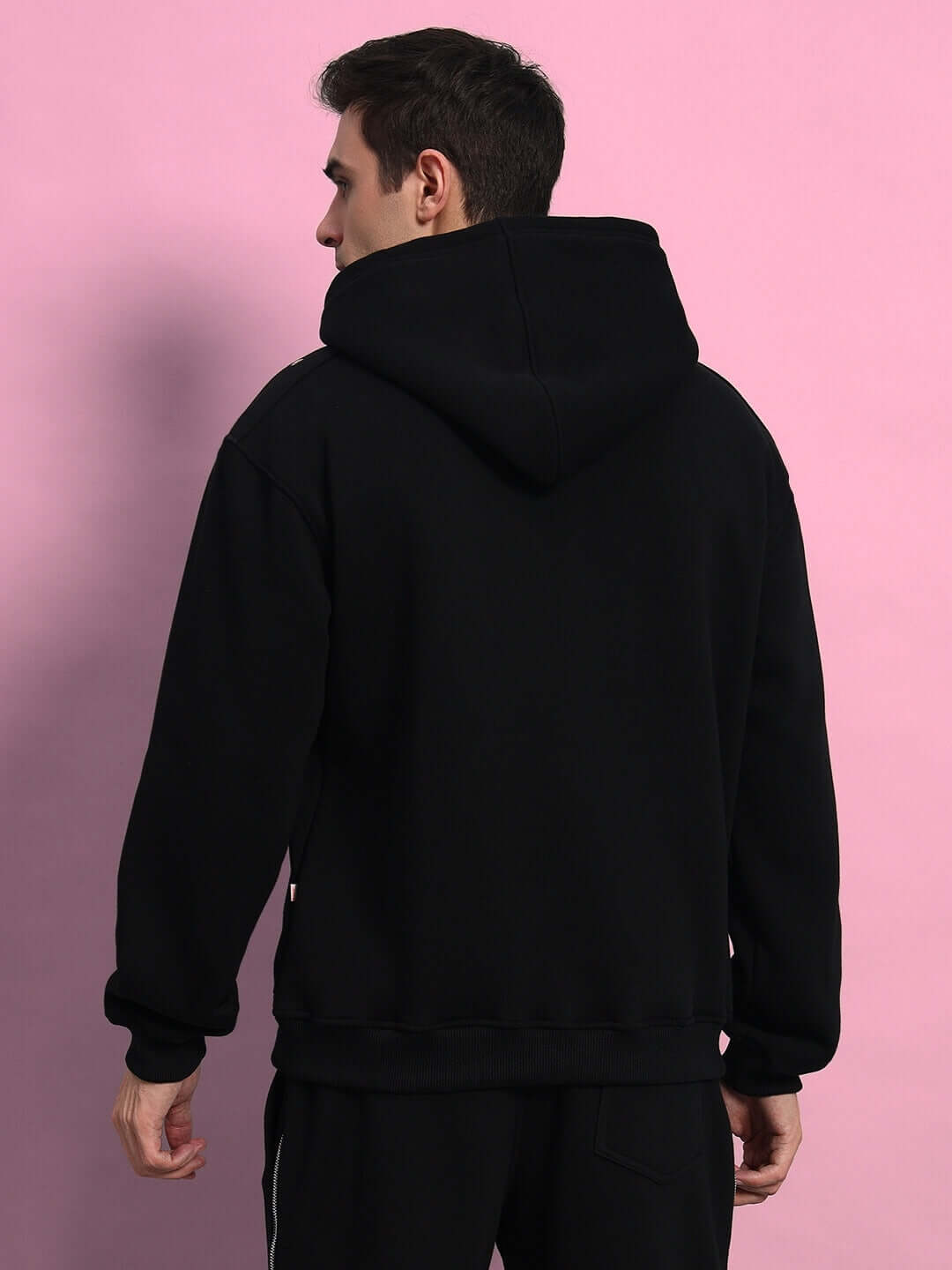 Back view of a person wearing a black Limitless Fleece Reflector Hoodie against a pink background.