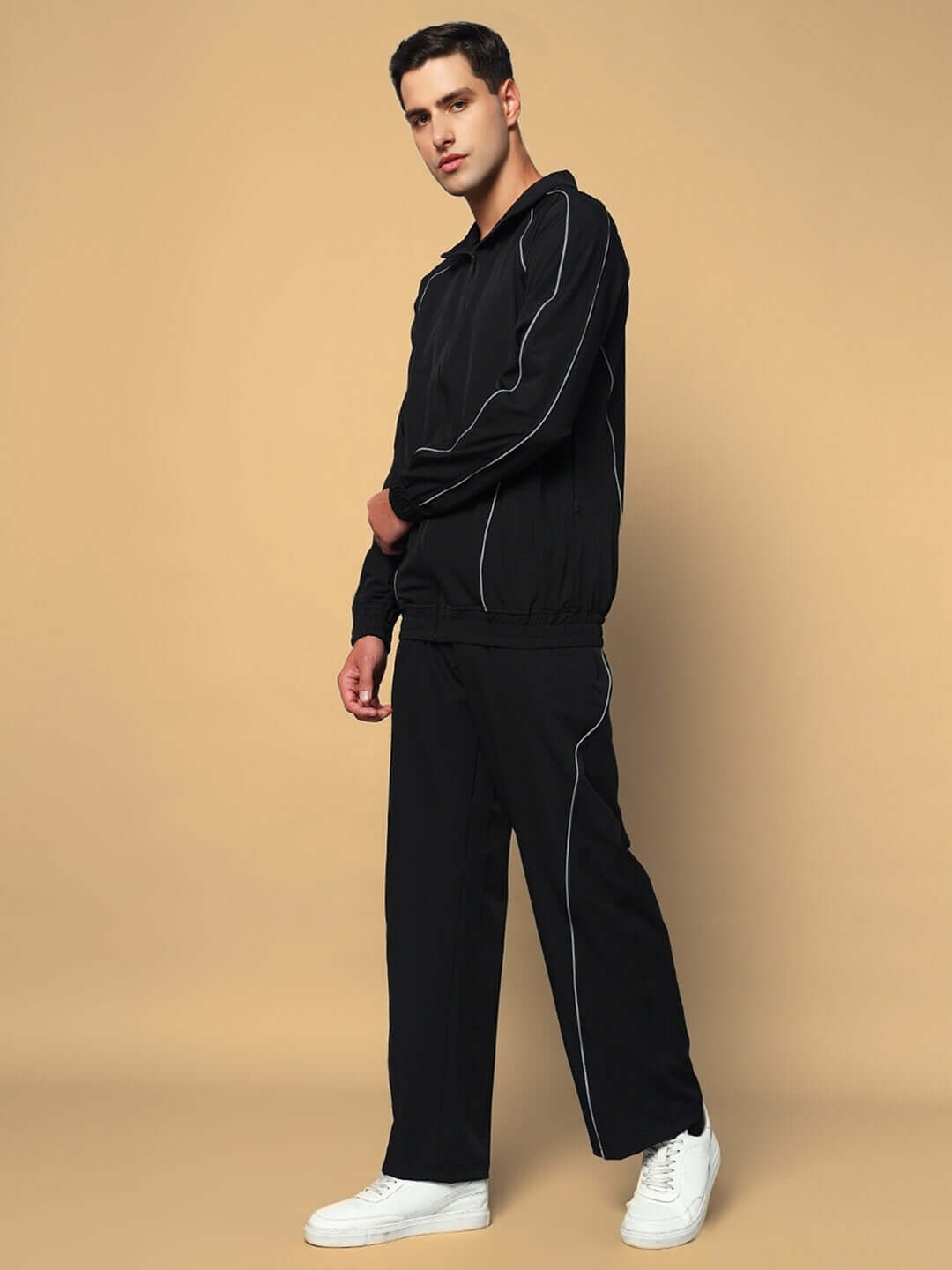 Man wearing black LOCO Reflector Parachute Cargo Pants with white sneakers, standing against a beige background.