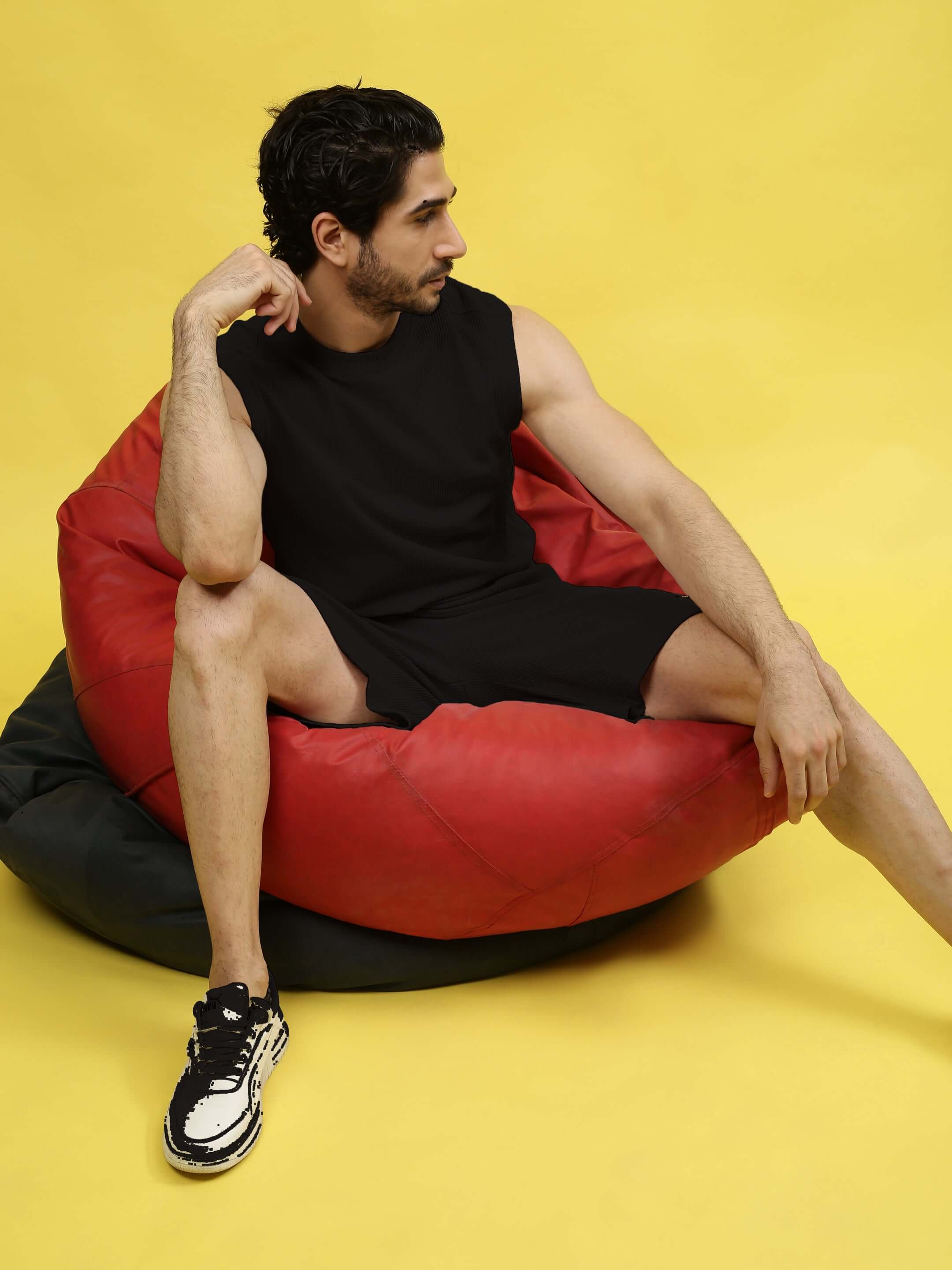 Man wearing LOW-KEY SOLID CO-ORD SET in black, sitting on a red bean bag, showcasing casual style in premium cotton fabric.