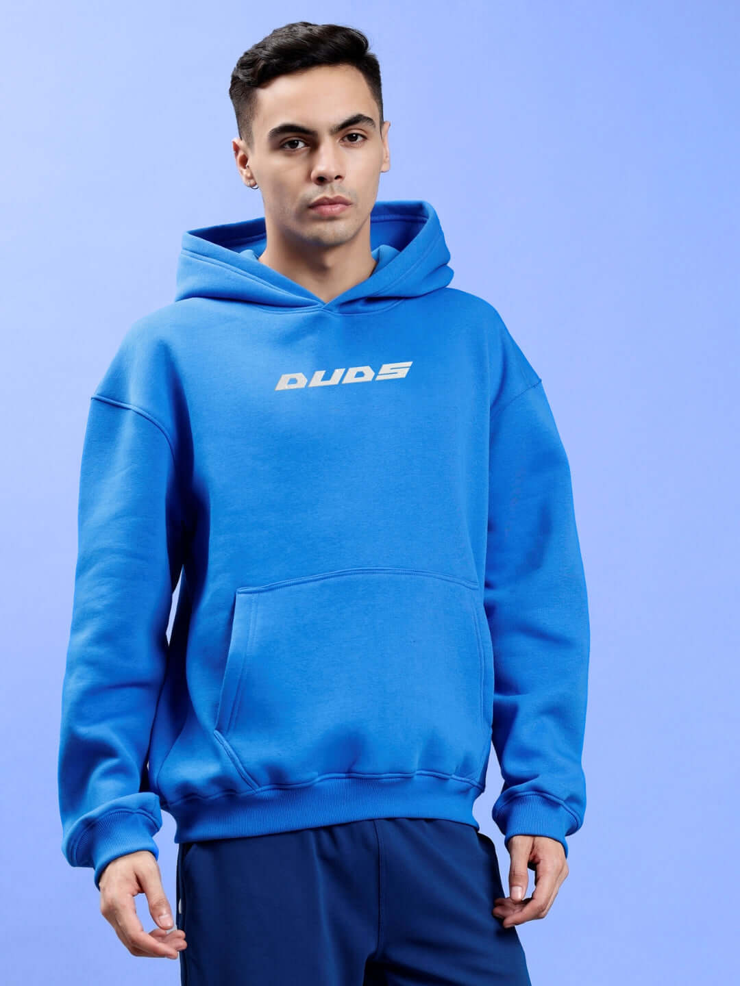 Man wearing LUNA FLECCE OVERSIZED HOODIE ROYAL BLUE with trendy design showcasing streetwear style against a light blue background.