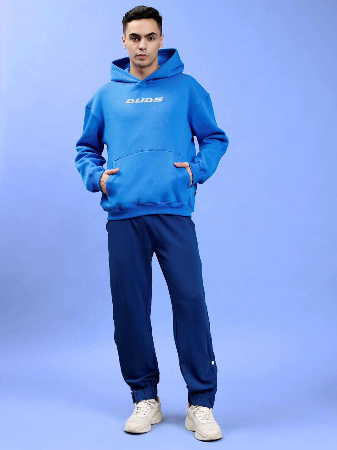 Man wearing LUNA FLECCE OVERSIZED HOODIE ROYAL BLUE, standing in stylish streetwear against a blue background.
