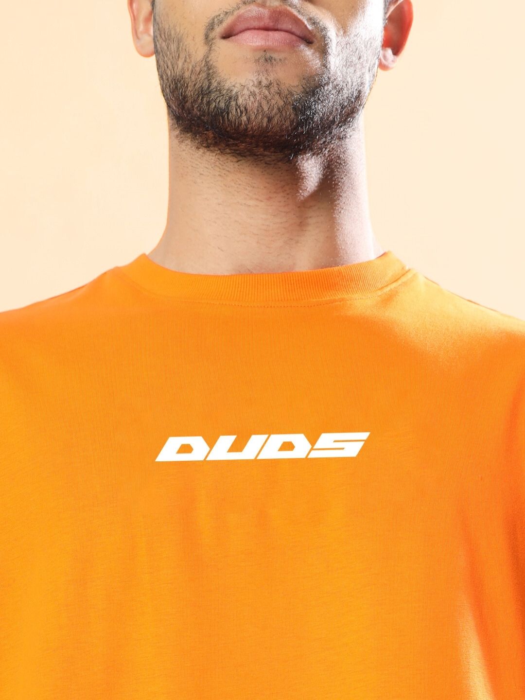 Man wearing MACLERAN PRINTED OVERSIZED T-SHIRT ORANGE with 'DUDS' text on chest