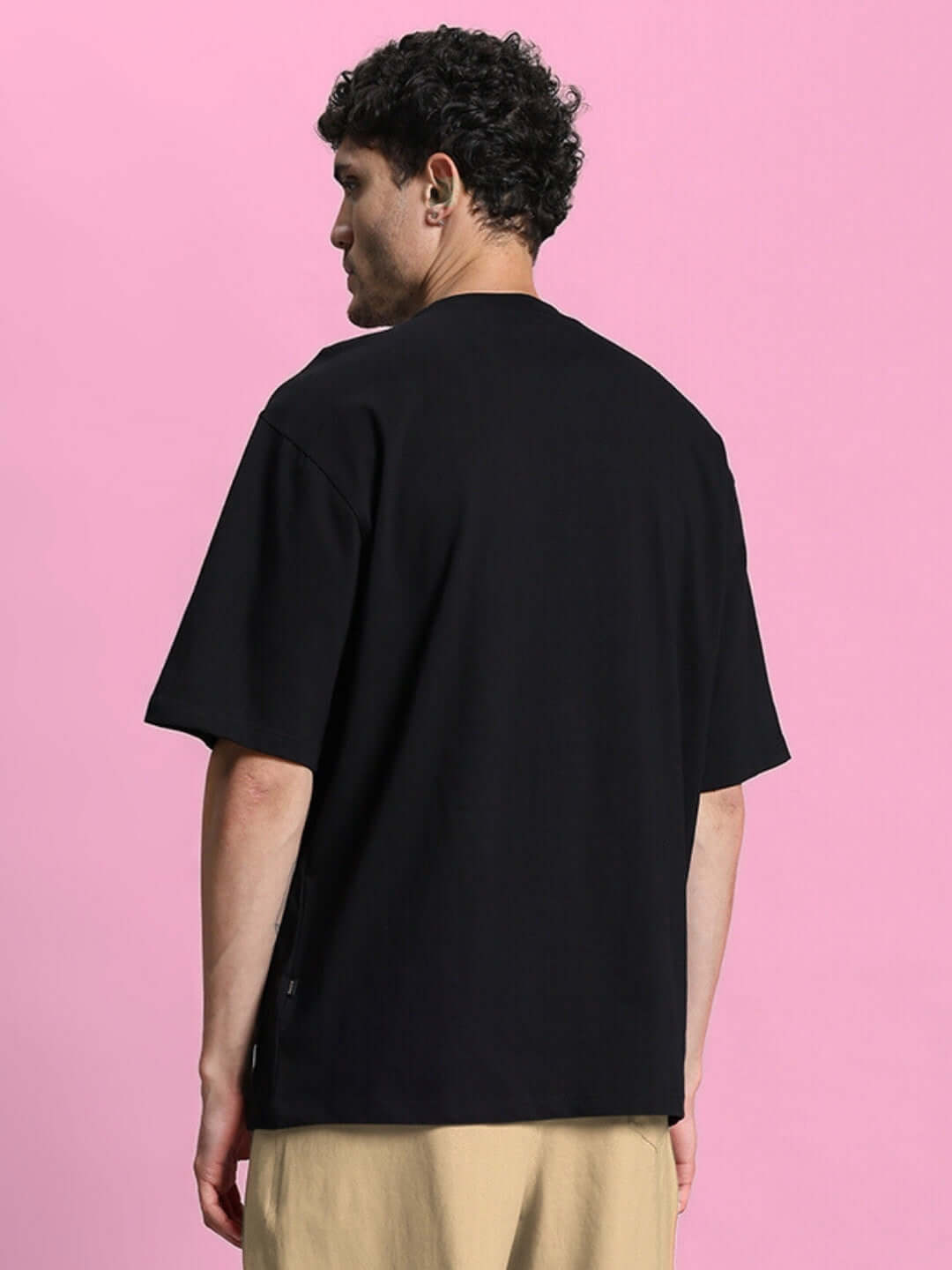 Back view of MAGIC CITY OVERSIZED T-SHIRT BLACK made from heavy gauge cotton fabric, worn by a model against a pink background.
