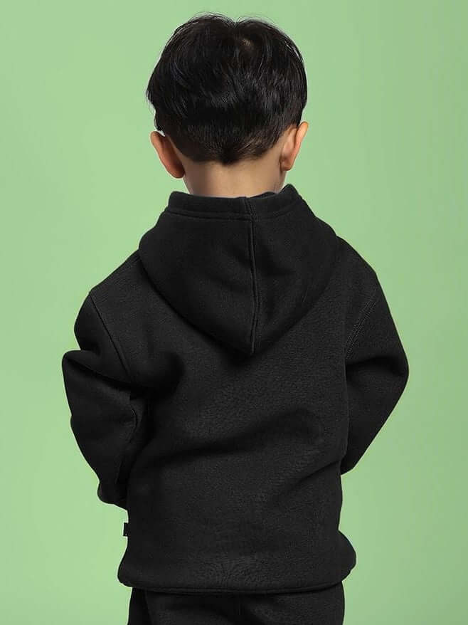 Young child wearing MAKE IT HAPPEN FLEECE HOODIE FOR BOYS AND GIRLS BLACK, showcasing the sleek design and cozy fabric on a green background.