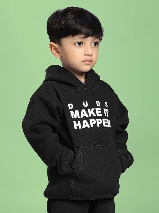 Child wearing MAKE IT HAPPEN FLEECE HOODIE FOR BOYS AND GIRLS BLACK on green background.