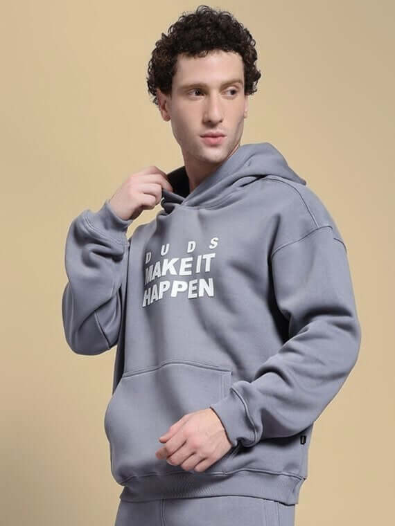 Man wearing the MAKE IT HAPPEN FLEECE HOODIE GREY with relaxed fit and adjustable drawstring hood.
