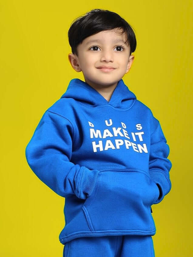 Child wearing MAKE IT HAPPEN FLEECE HOODIE FOR BOYS AND GIRLS ROYAL BLUE, standing with hands in pockets, yellow background