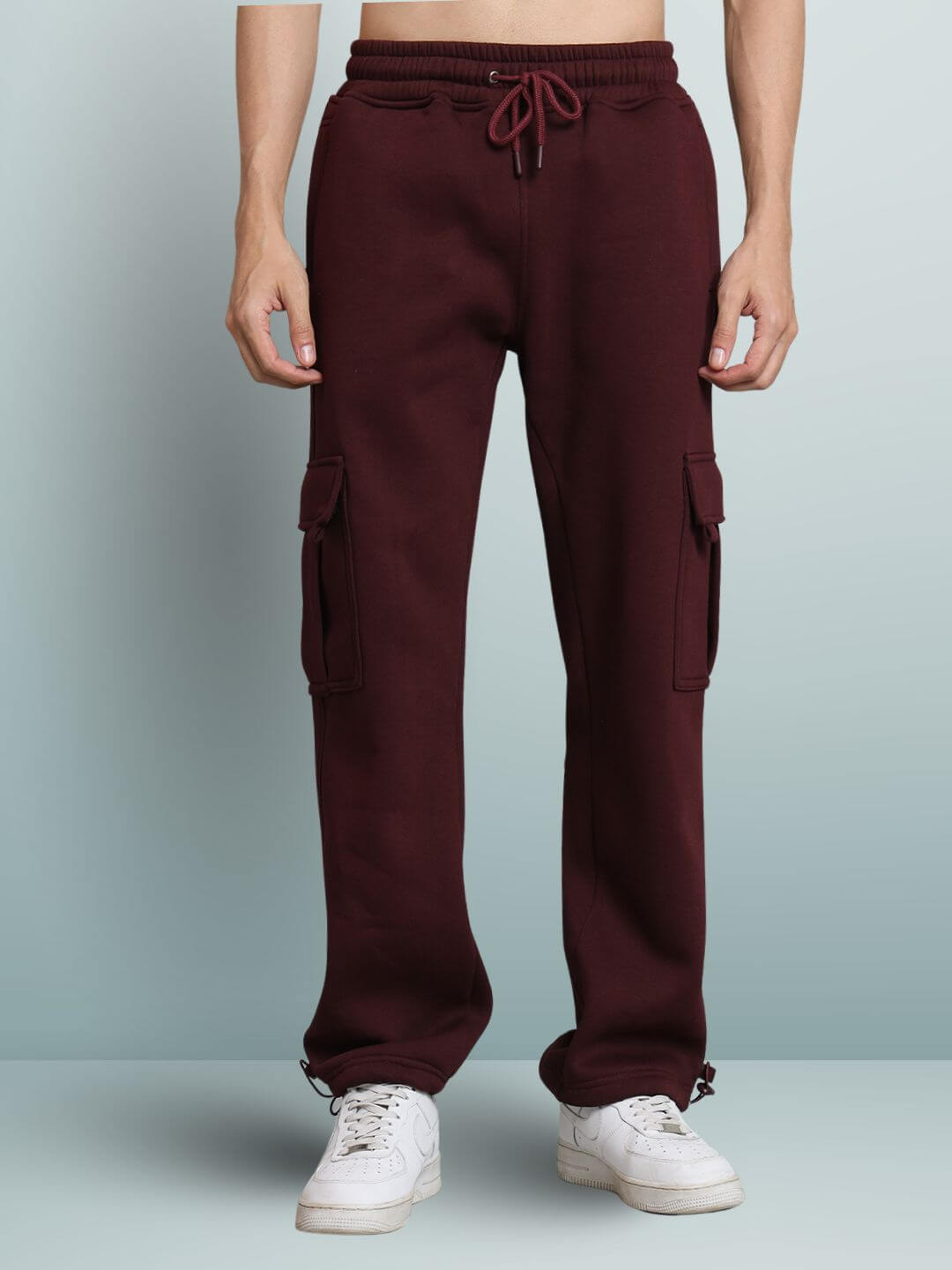 Model wearing maroon relaxed fit cargo fleece pants with drawstring waist and side pockets.