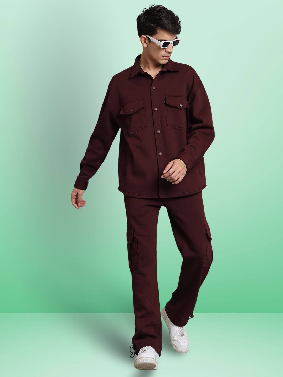 Model wearing maroon relaxed fit full sleeves fleece overshirt with matching pants and white sneakers, styled with sunglasses.