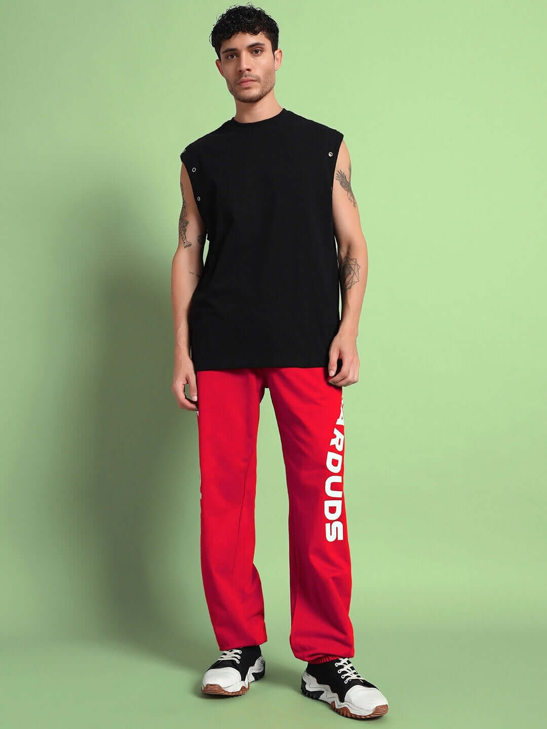 Man wearing Ellen Relaxed Fit Jogger in red, paired with a black sleeveless top, showcasing a bold casual style against a green background.