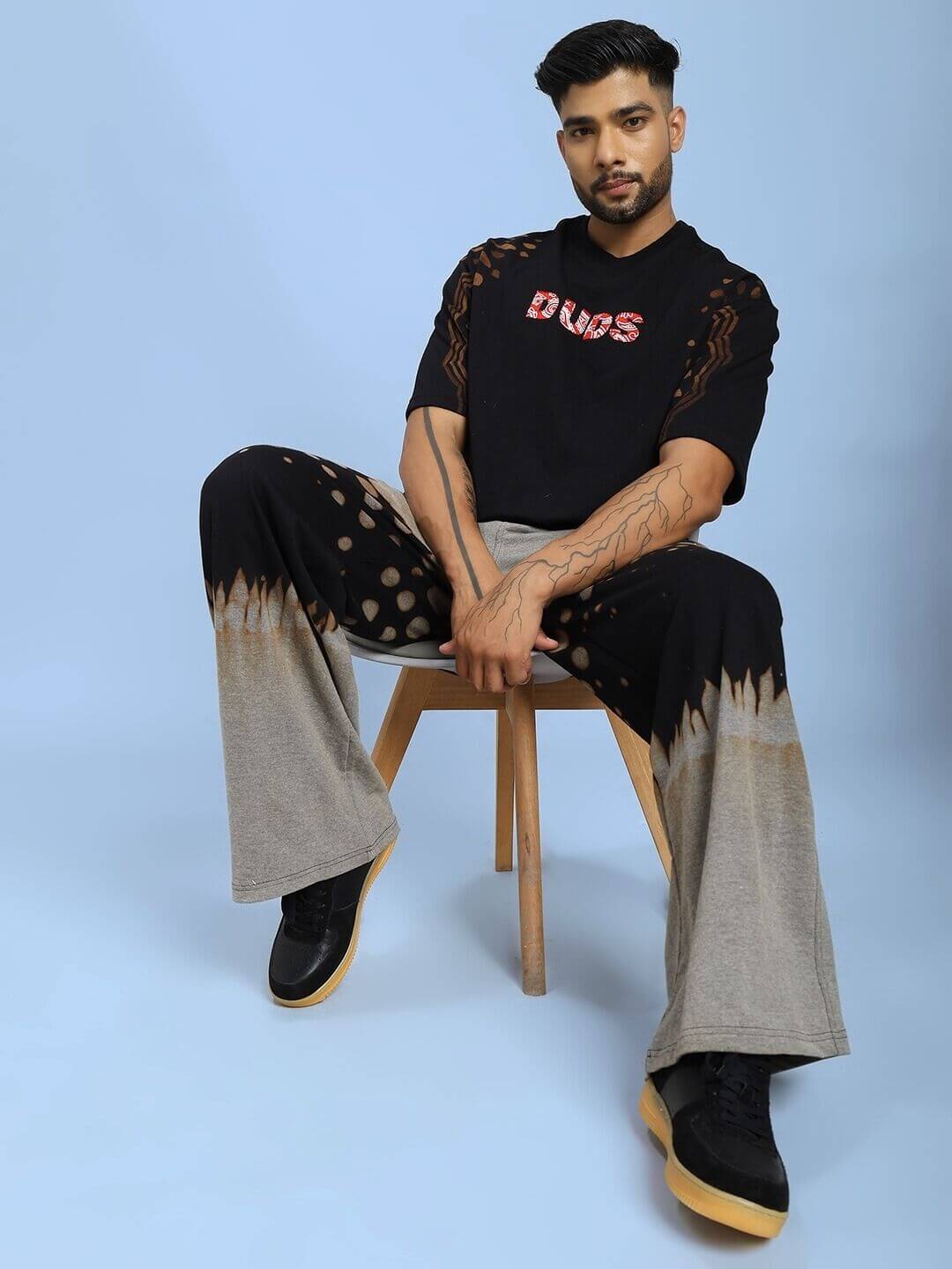 Man modeling SHADOW SWIRL TIE-DYE T-SHIRT BLACK with stylish pants, showcasing casual style on blue background.