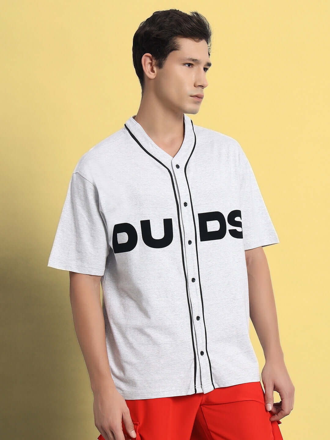 Man wearing Zing Raglan oversized melange grey t-shirt with mandarin collar, featuring "DUDS" logo, against a yellow background.