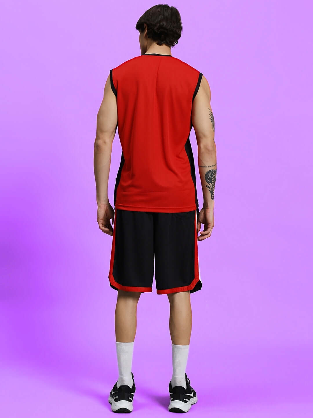 Man wearing PORTIA REGULAR FIT SHORTS BLACK with red top on purple background, showcasing comfortable athletic wear.