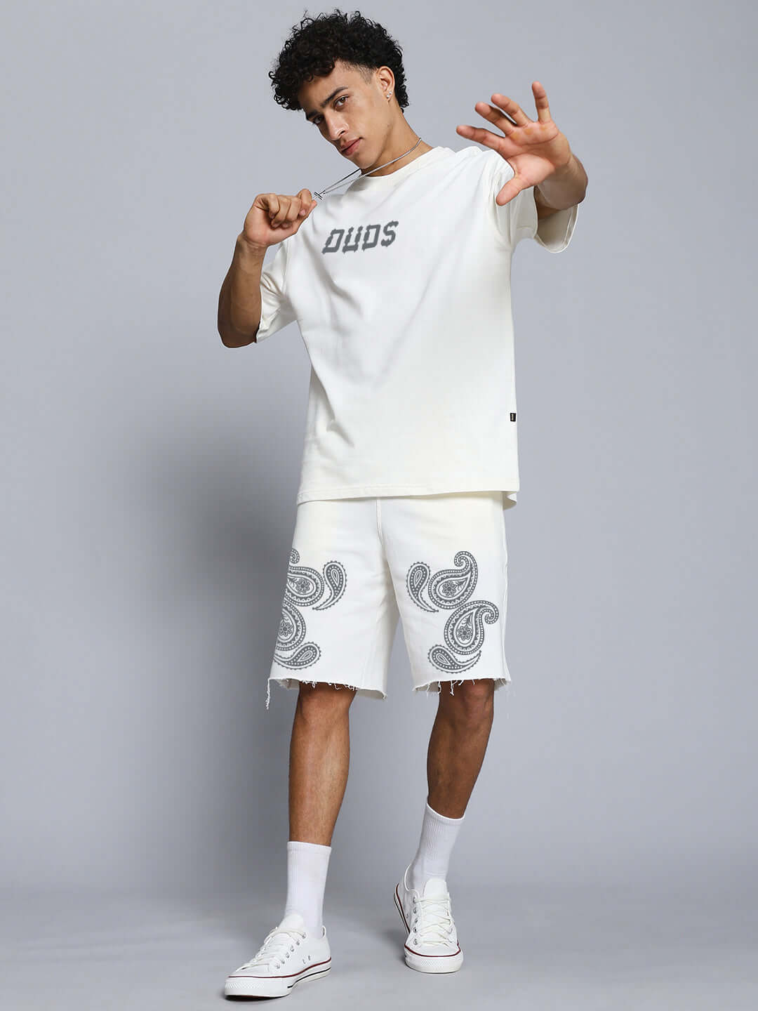 Man wearing MESSI PAISLEY PRINT OVER-SIZED T-SHIRT OFF WHITE with paisley shorts, showcasing casual street style against a gray background.
