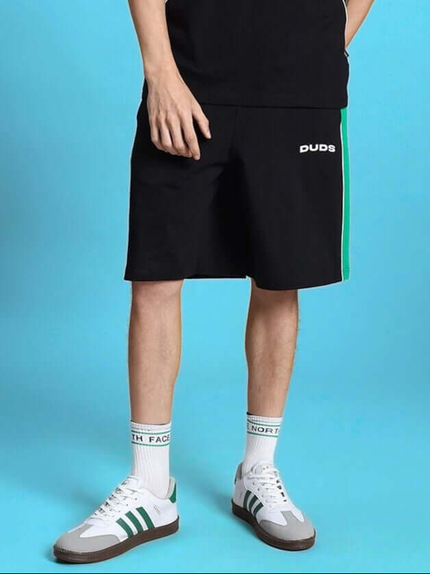 Model wearing METEORIC REGULAR FIT SHORTS BLACK with green stripe detail from WEAR DUDS, ideal summer streetwear for men and women.