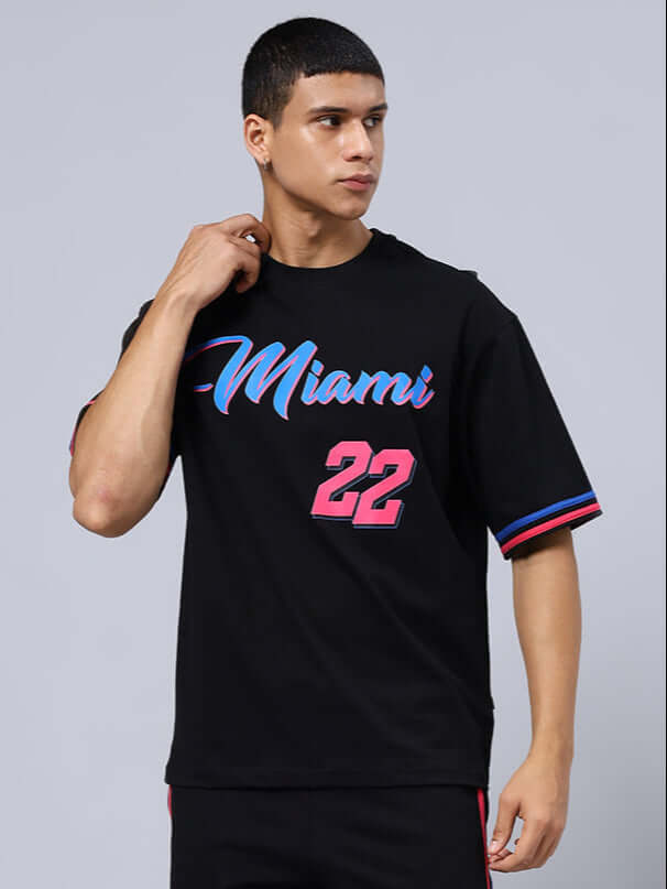 Model wearing MIAMI OVER-SIZED T-SHIRT BLACK with vibrant Miami lettering and number 22, showcasing casual streetwear style.