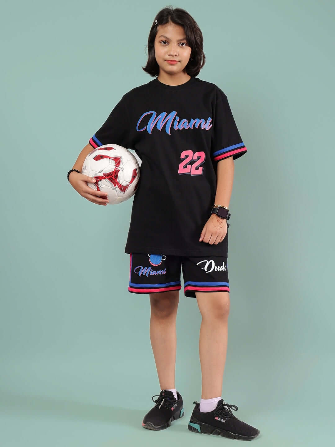 Child wearing MIAMI SHORTS FOR BOYS & GIRLS BLACK holding a soccer ball, featuring colorful lettering and sporty design.