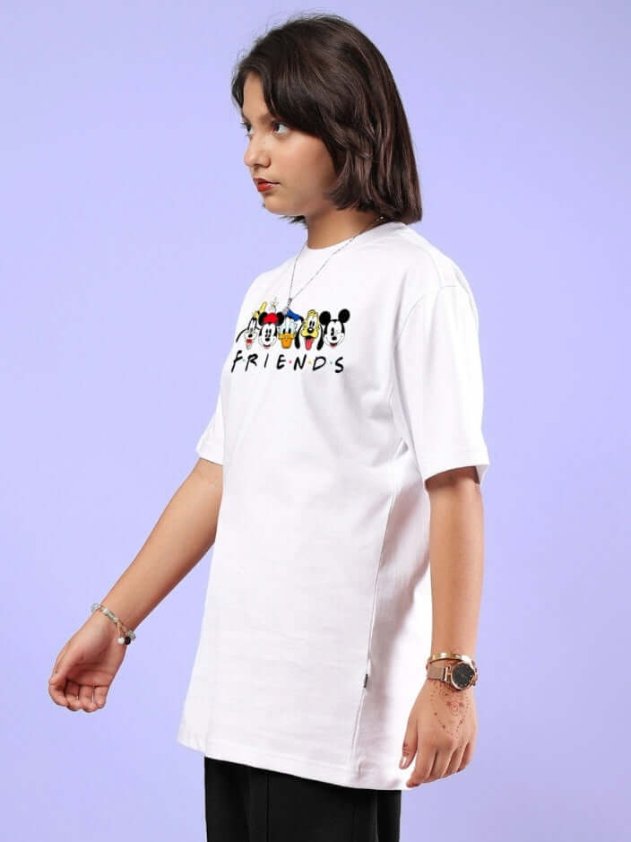 Child wearing MICKEY AND FRIENDS T-SHIRT FOR BOYS & GIRLS WHITE with colorful character print, side view against purple background.