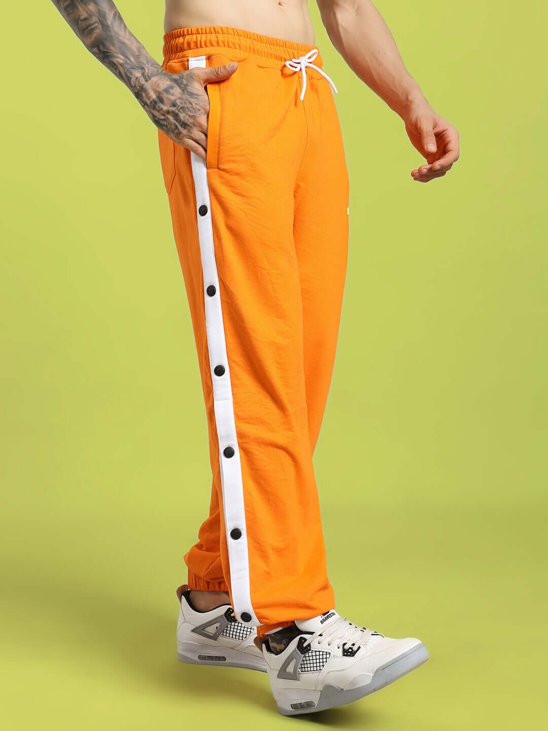 Person wearing MILLER RELAXED FIT JOGGERS ORANGE with button details and sneakers, showcasing streetwear style.