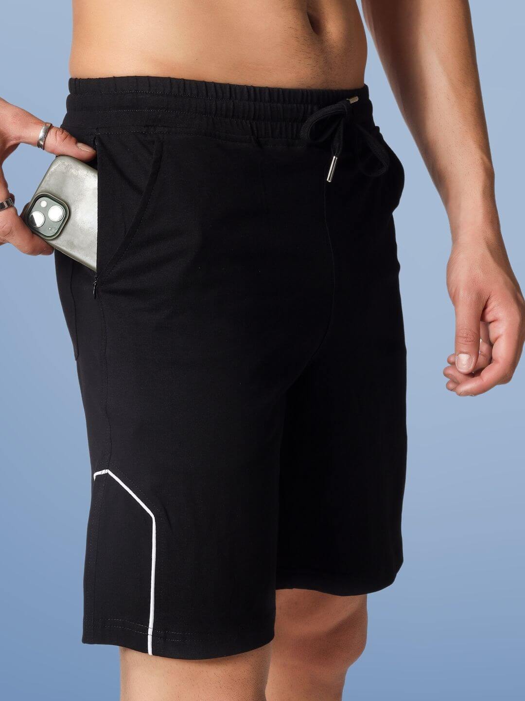 Man wearing black minimal shaped shorts with custom fit option, holding phone in pocket, showcasing regular fit style.