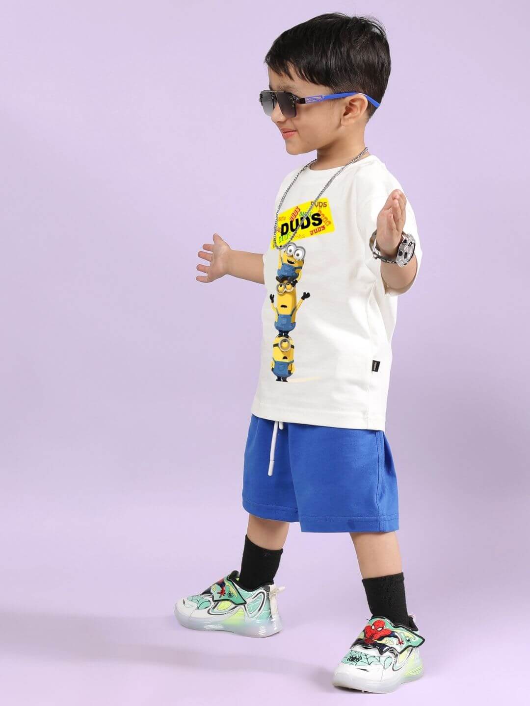 Child wearing Minion cartoon co-ord set with white t-shirt and blue shorts, accessorized with sunglasses and colorful sneakers.