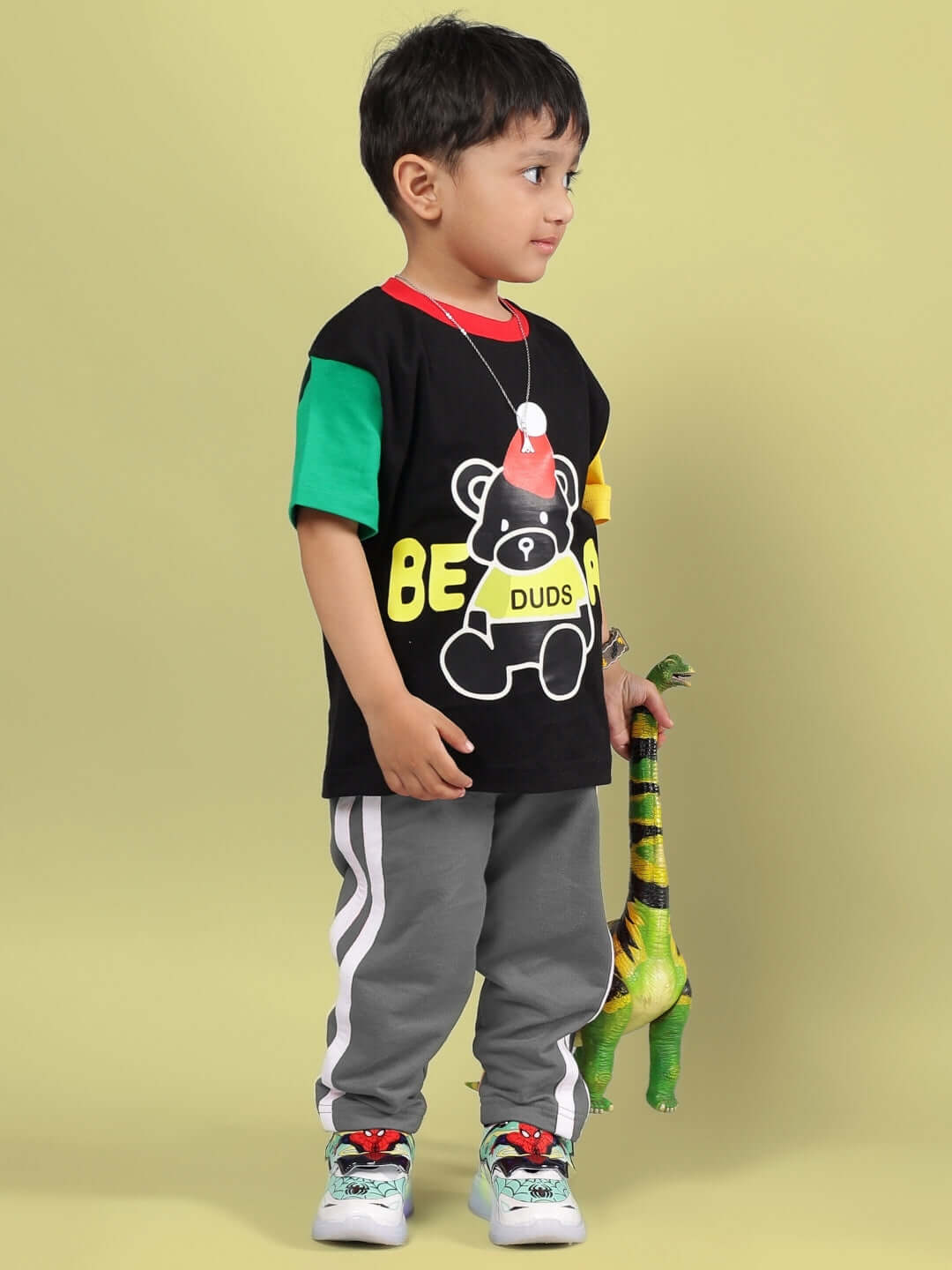 Young boy wearing MOCHA CO-ORD FOR BOYS & GIRLS BLACK GREY outfit featuring colorful t-shirt and grey pants, holding a green toy dinosaur.