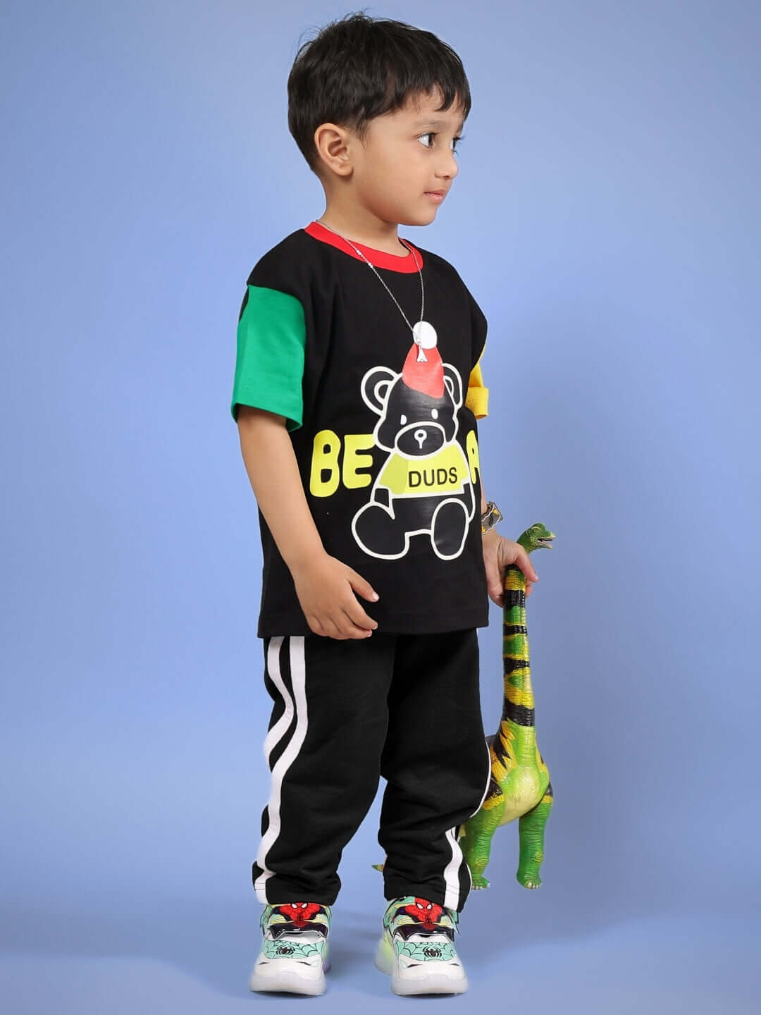 Child wearing MOCHA CO-ORD FOR BOYS & GIRLS BLACK outfit, standing with a green dinosaur toy, featuring colorful DUDS bear print shirt.