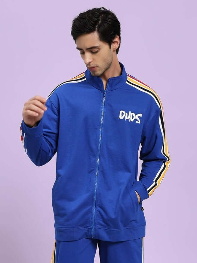 MODERN EDGE MULTI-STRIPE JACKET ROYAL BLUE Man wearing a blue tracksuit with colorful stripes on a light purple background