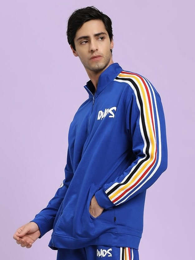 MODERN EDGE MULTI-STRIPE JACKET ROYAL BLUE Man wearing a blue tracksuit with colorful stripes on a light purple background