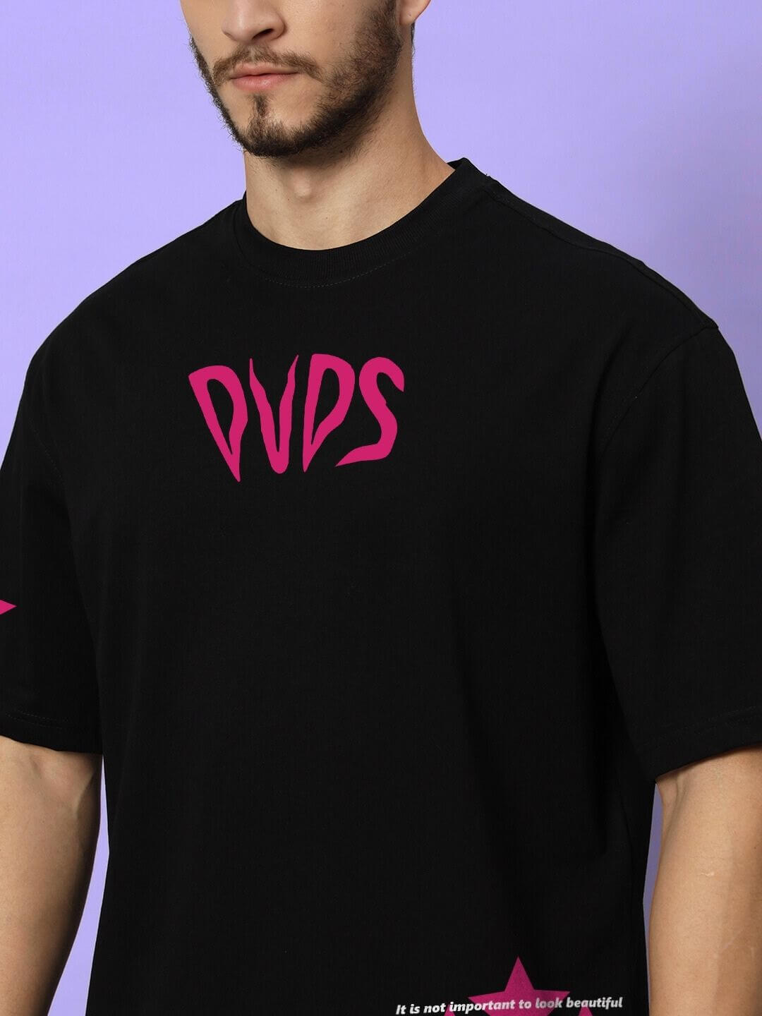 Close-up of a man wearing a MODERN LOVE OVER-SIZED T-SHIRT BLACK with bold pink graphics on a purple background.