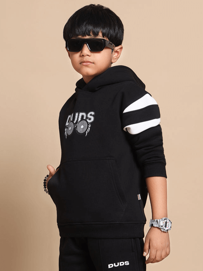 Child wearing MOLLY oversized black hoodie with white stripes, featuring unique design by DUDS, sunglasses, watch, and bracelet.