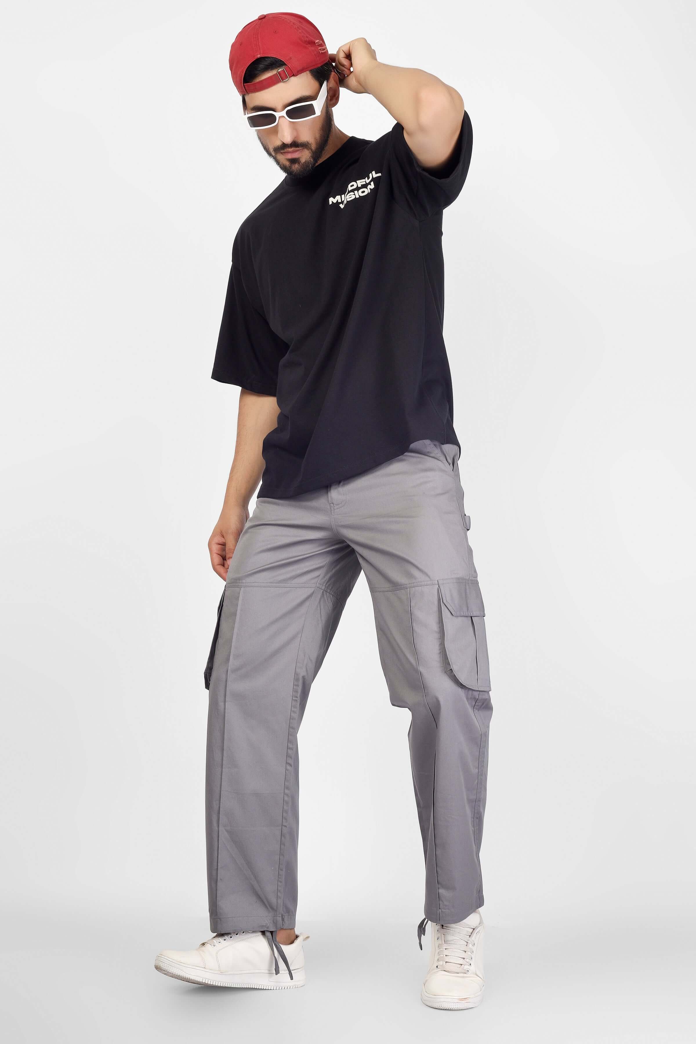 Man wearing moon stone cargo pants with 6 pockets, paired with a black t-shirt, red cap, and sunglasses. Casual streetwear style.