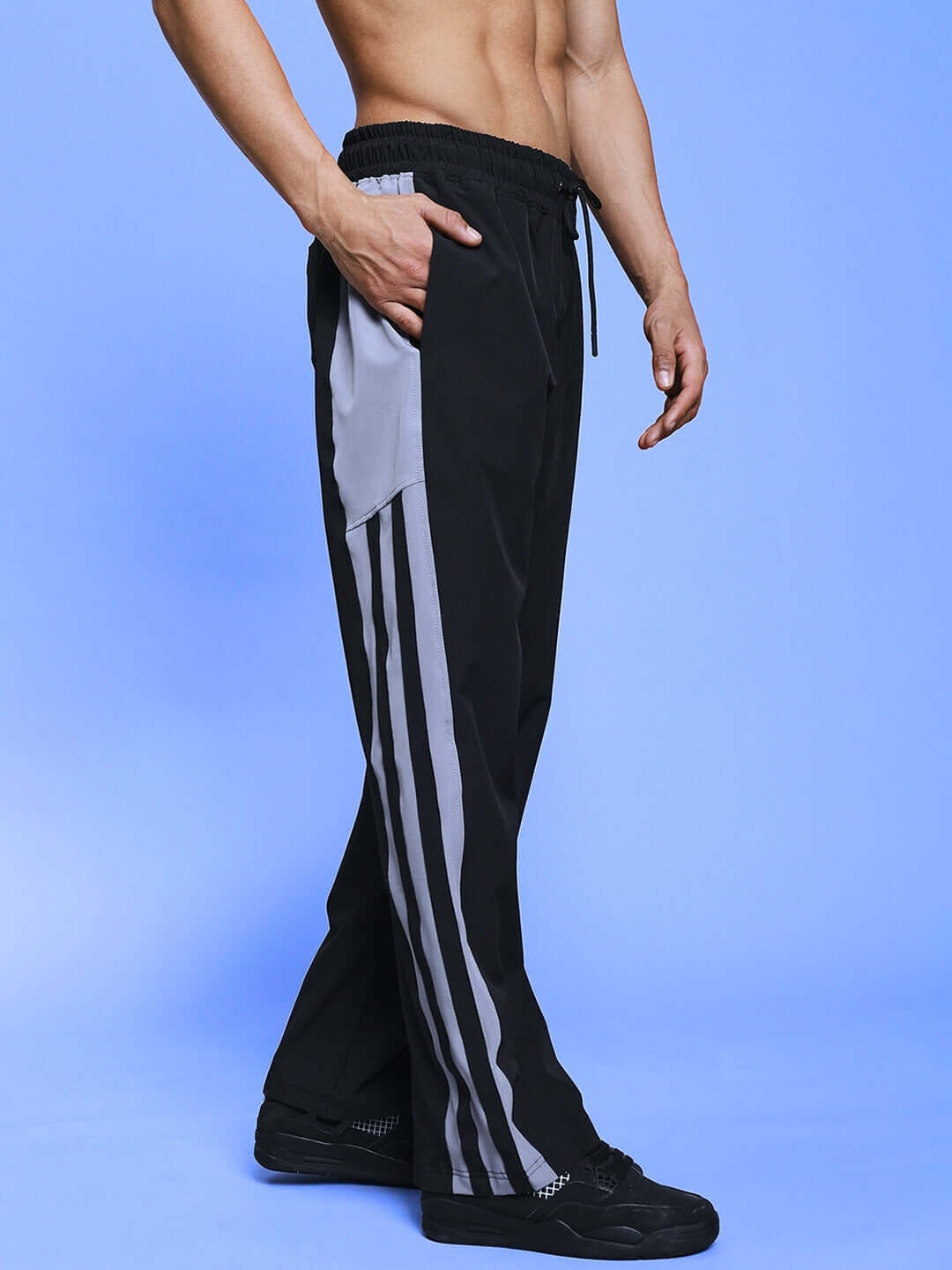 Side view of black Morgan Relaxed Fit Cargo Pant with gray pocket details and stripes, shown on a male model against a blue background.