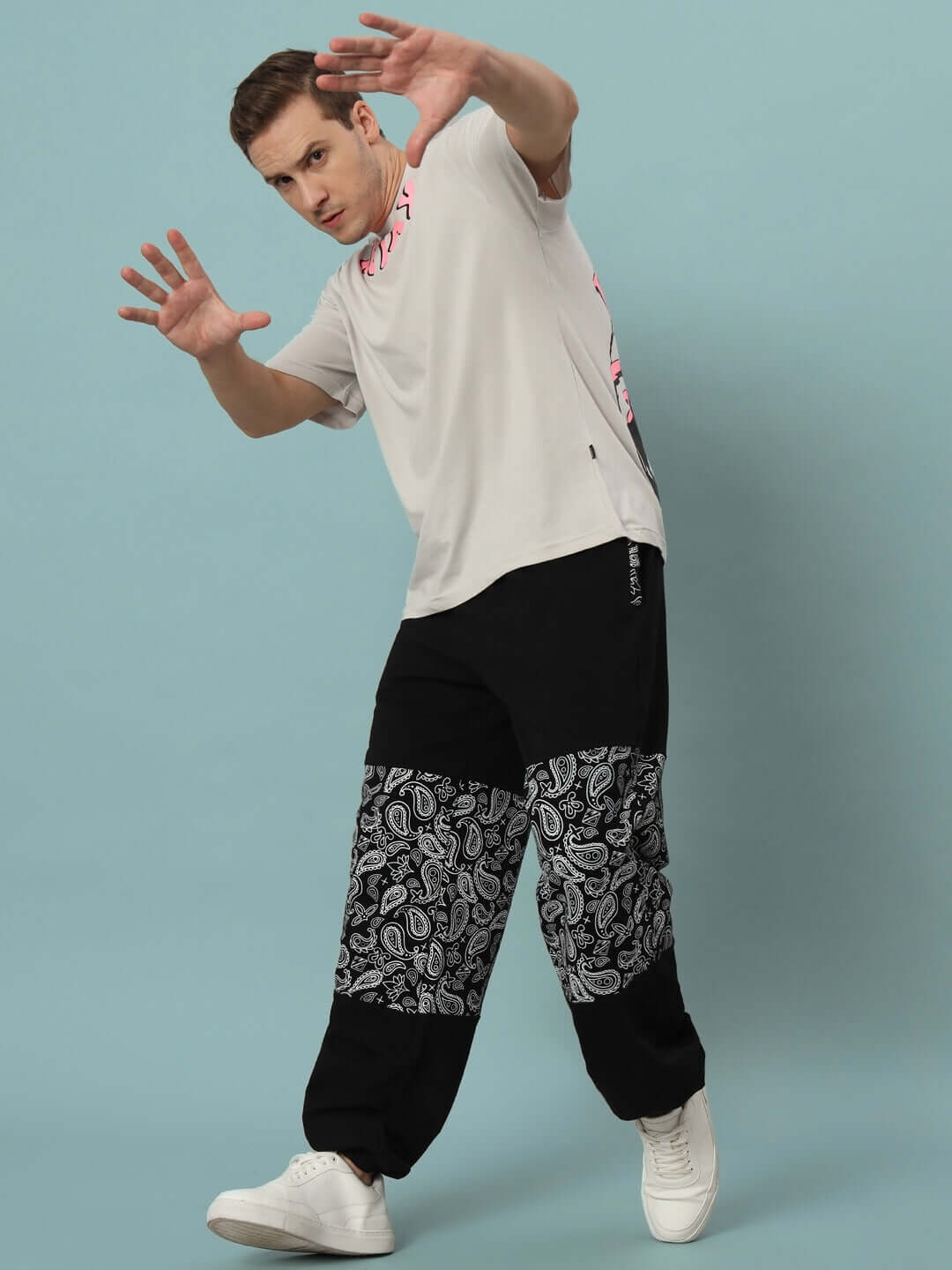 Model wearing mosaic baggy joggers in black with artistic pattern, showcasing comfort and style on a light blue background.