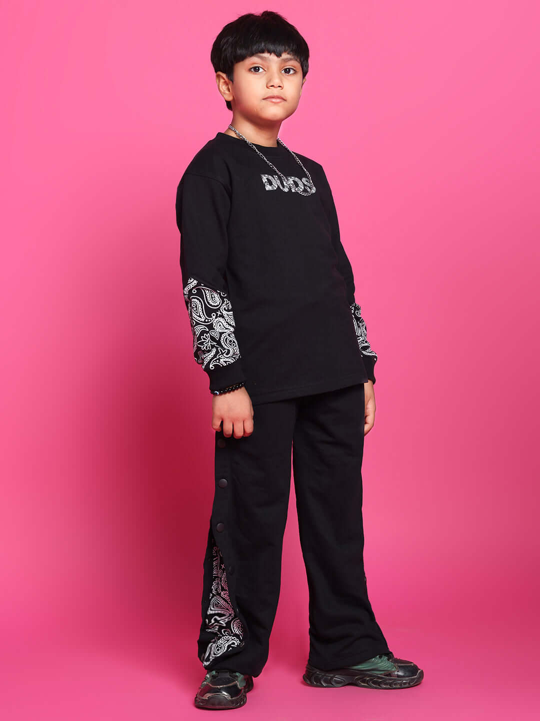 Child wearing black motif co-ord set by DUDS, showcasing comfortable and stylish design for boys and girls against a pink background.