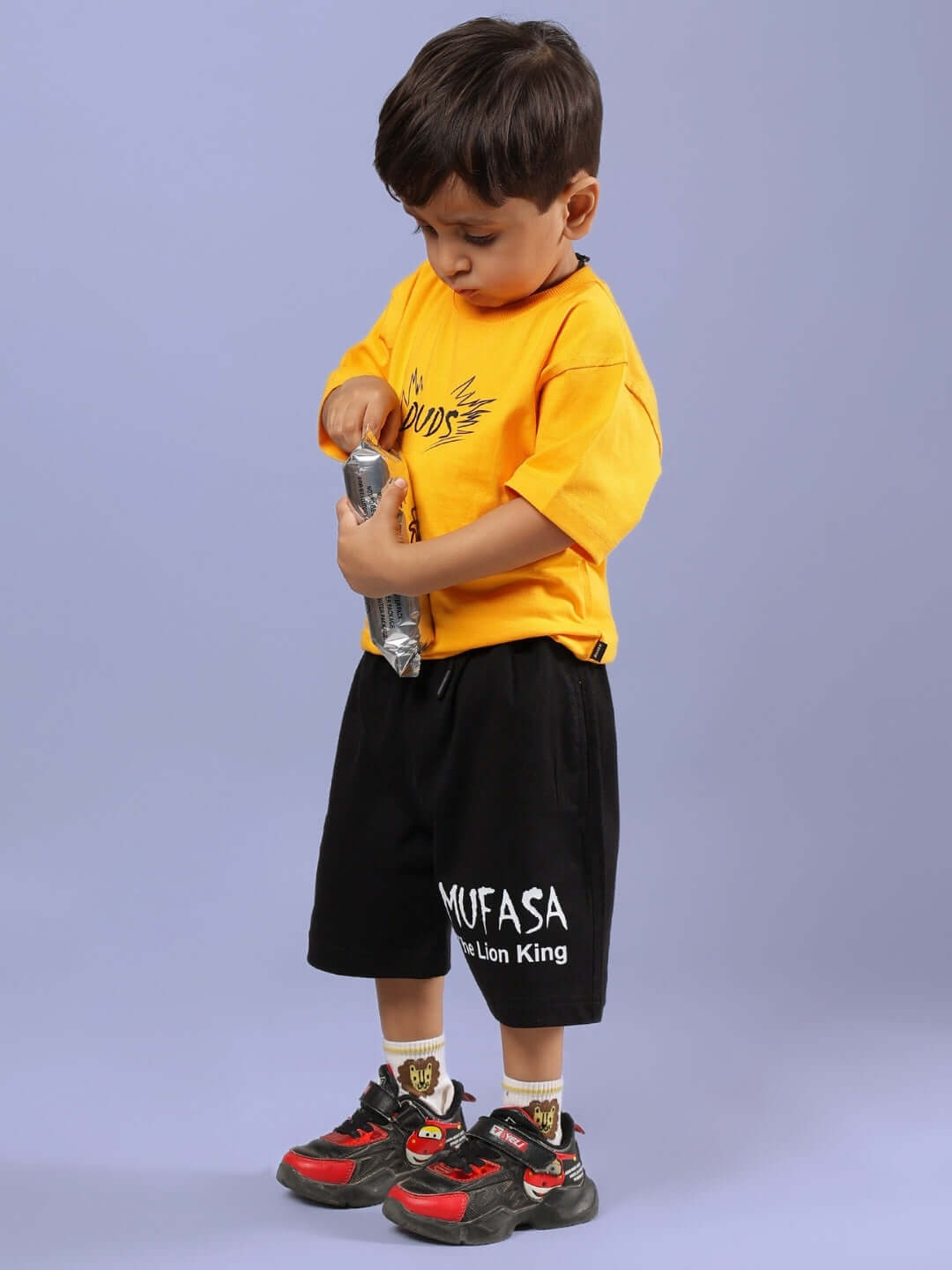 Young child wearing MUFASA SHORTS FOR BOYS & GIRLS BLACK, standing with a bottle in hand.