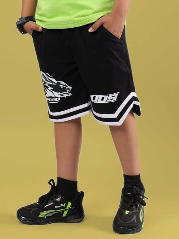 Child wearing MUFFIN SHORTS FOR BOYS & GIRLS BLACK with athletic shoes and green shirt, showcasing casual style.