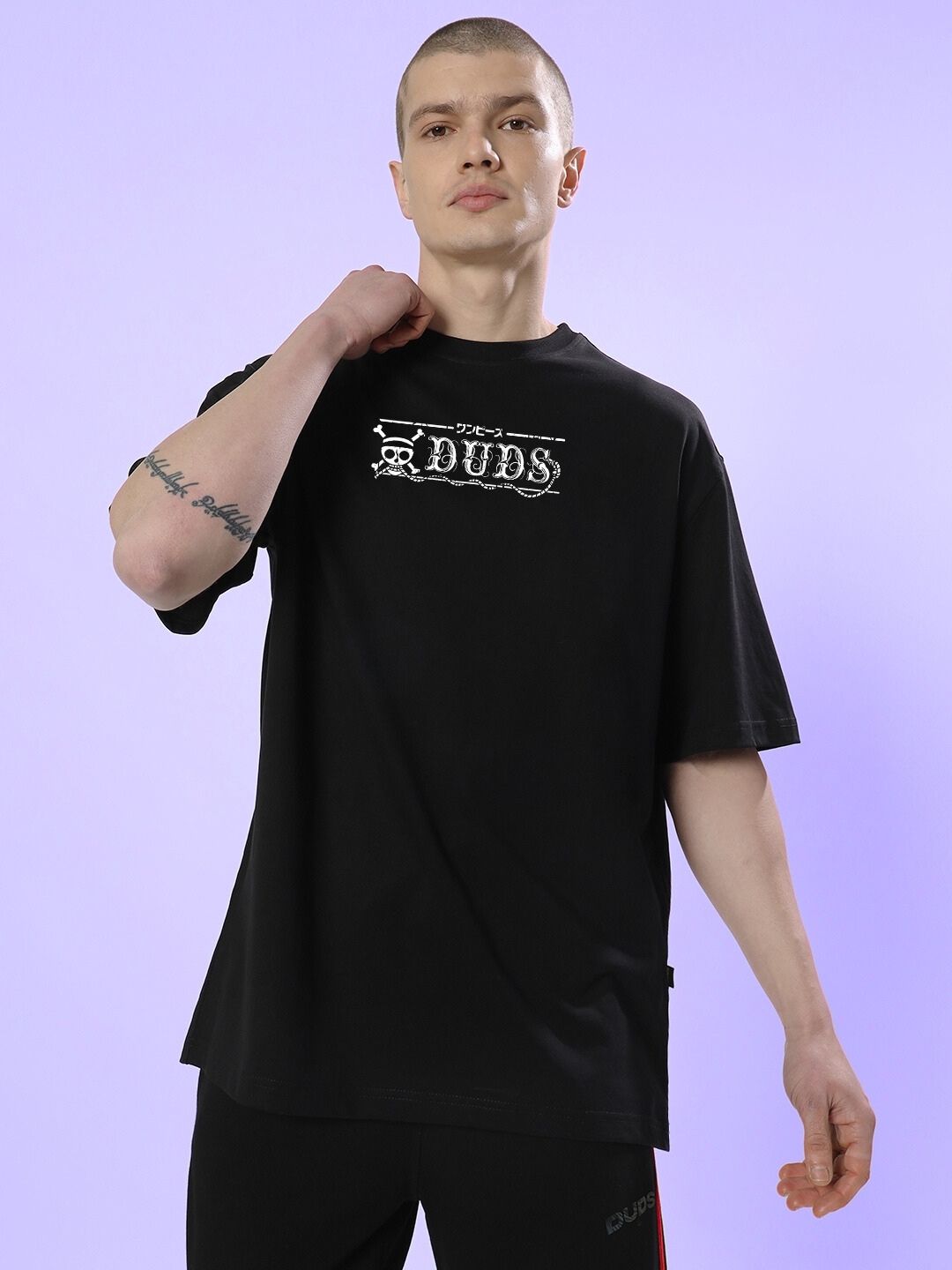 Model wearing MUGIWARA PRINTED OVERSIZED T-SHIRT BLACK in a casual pose against a purple background