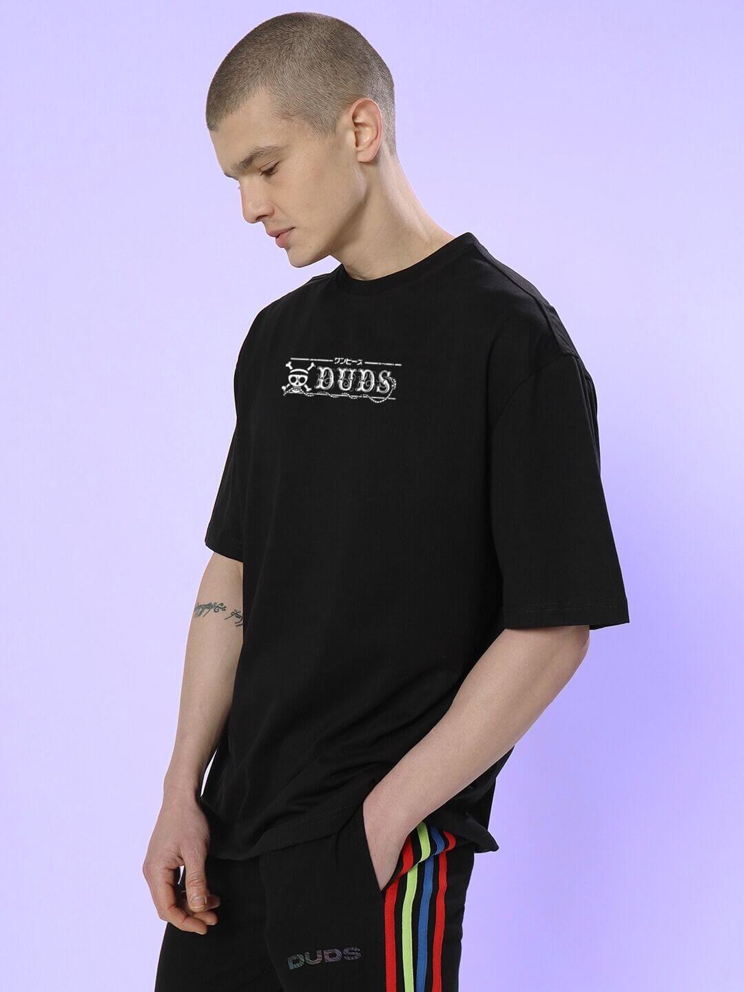 Person wearing Mugiwara Printed Oversized T-shirt Black in streetwear style with colorful side stripe pants.