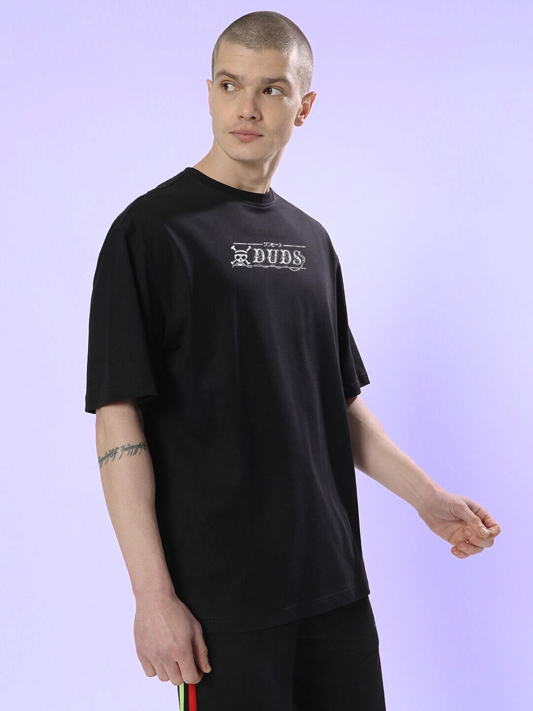 Man wearing a MUGIWARA PRINTED OVERSIZED T-SHIRT BLACK against a light purple background, showcasing streetwear style.