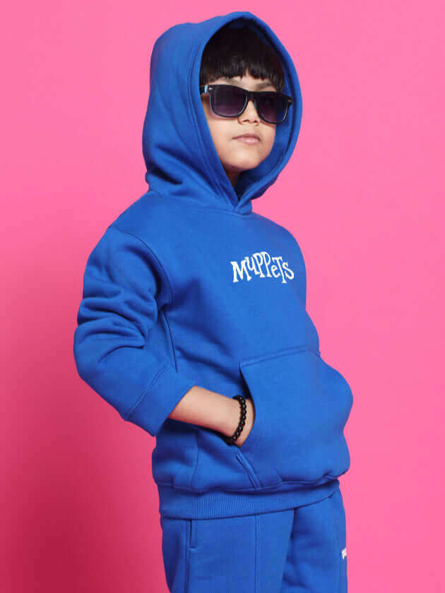 Child wearing blue Muppets co-ord set with hoodie and pants in front of pink background.