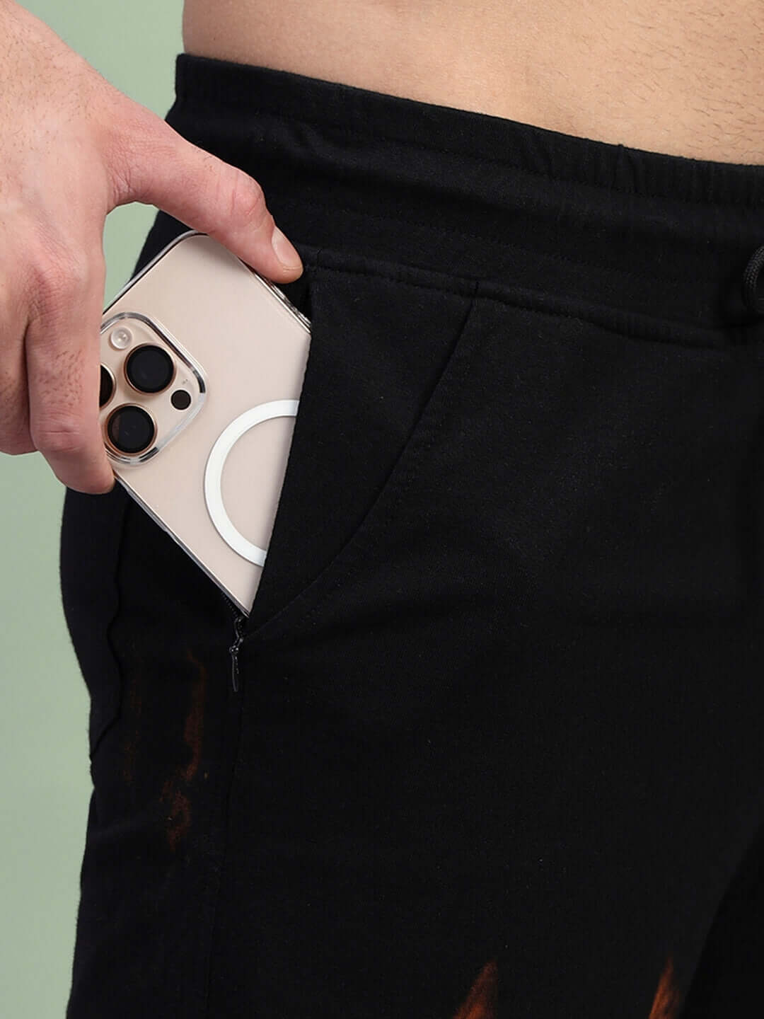 Close-up of a hand placing a smartphone into the pocket of a black tie-dye muscle tee co-ord set, showing stretch fabric detail.