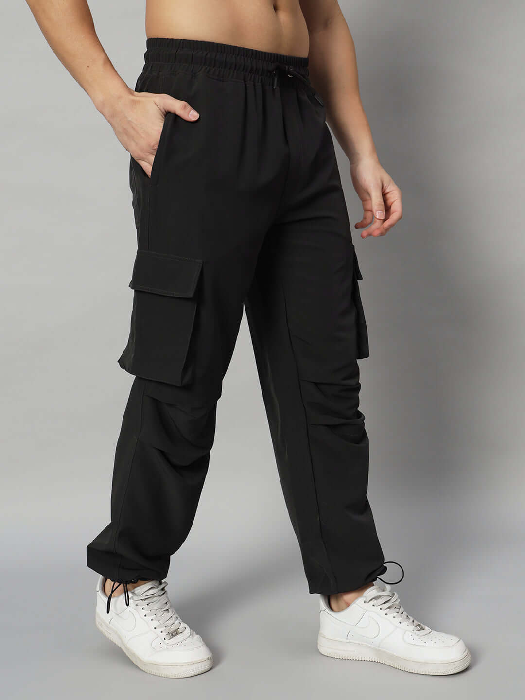 Black relaxed fit cargo pants with side pockets, worn by a person with one hand in pocket, paired with white sneakers. Ideal for custom fit.