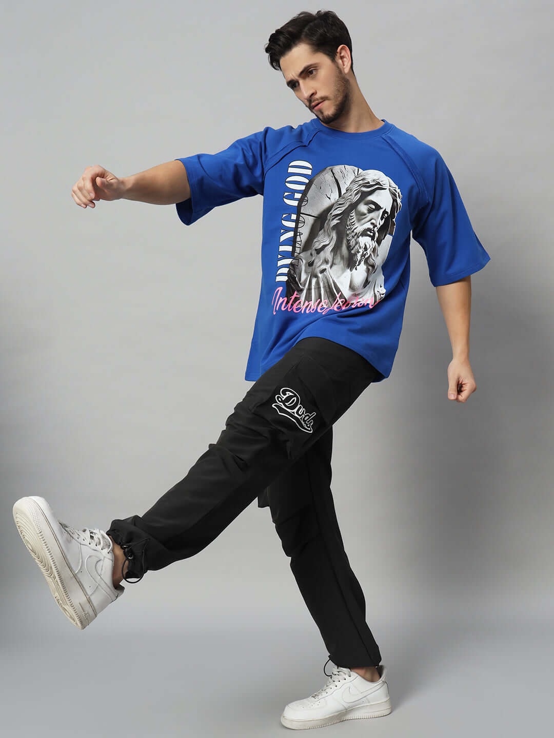Model wearing Myriad Relaxed Fit Cargo Pants in black, styled with a blue graphic tee and white sneakers, showcasing casual style.