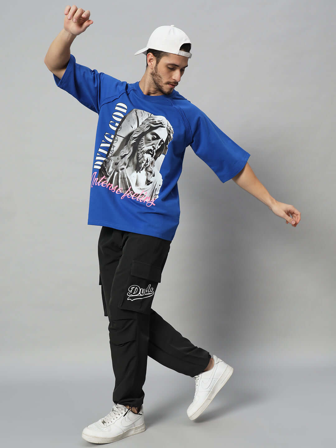 Model wearing MYRIAD Relaxed Fit Cargo Pants in black, paired with a blue graphic tee and white cap, showing casual style and comfort.