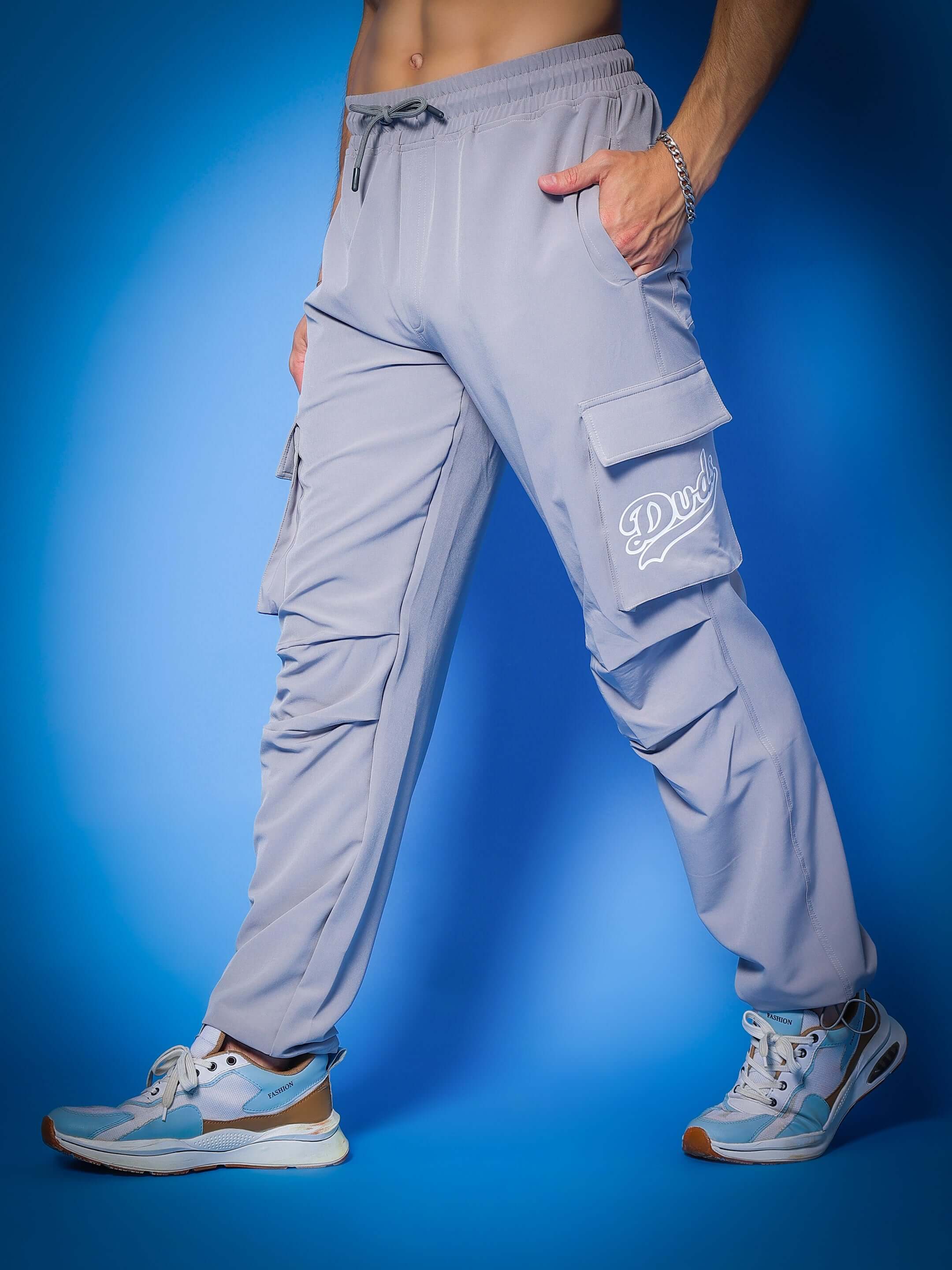 Stylish grey relaxed fit cargo pants with pockets, worn by model standing on blue background - customizable and handmade by DUDS.