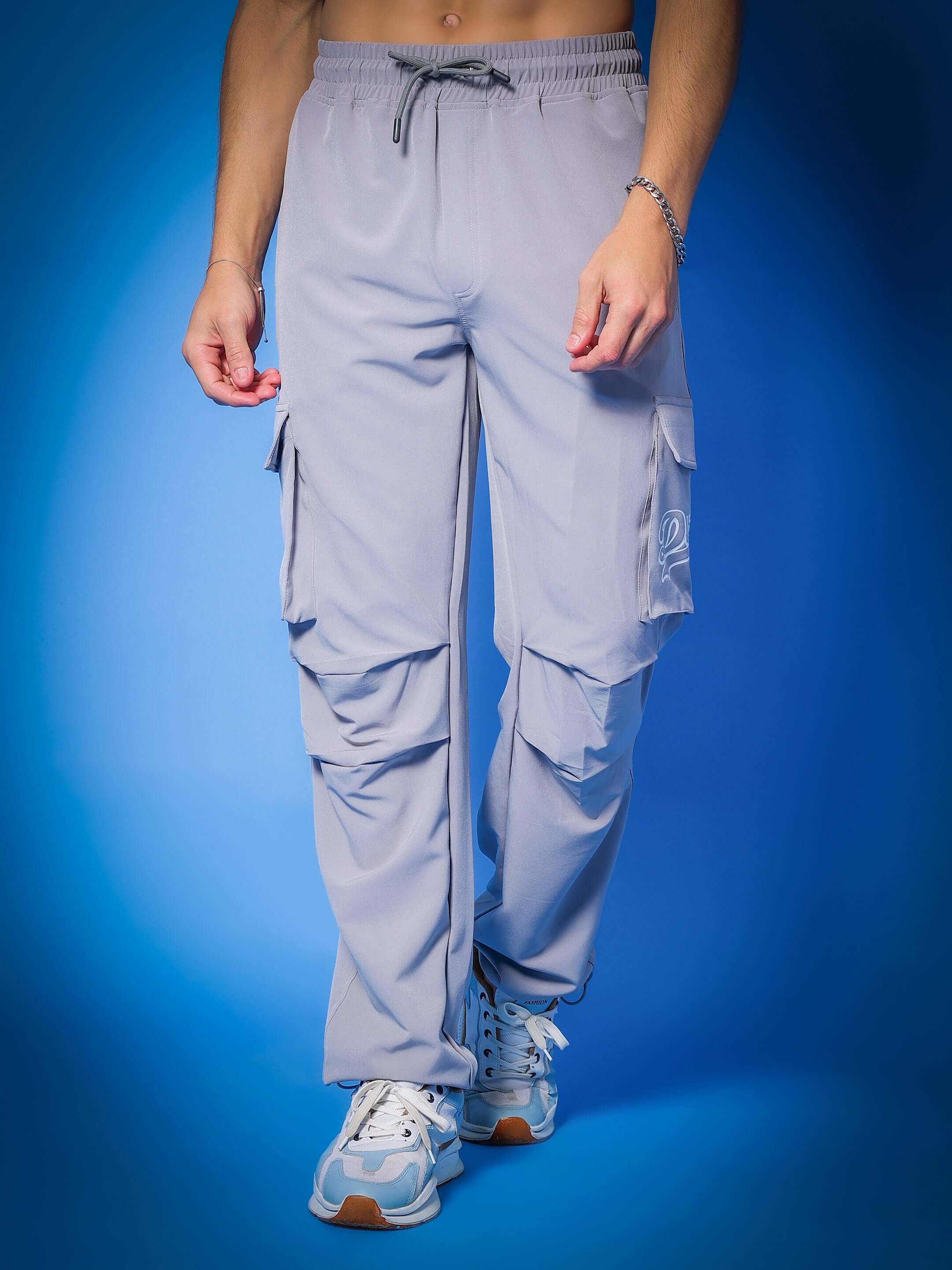 Model wearing Myriad Relaxed Fit Cargo Pants in grey, featuring multiple pockets and drawstring waist, on a blue background.